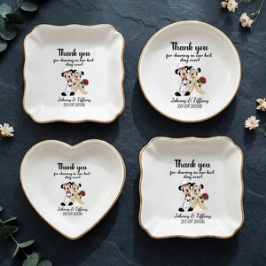 Puede incluir: Cuatro platos de cer&aacute;mica blanca con bordes dorados, cada uno con una forma diferente: cuadrado, redondo, coraz&oacute;n y un cuadrado con bordes festoneados. Cada plato tiene un gr&aacute;fico de boda de Mickey y Minnie Mouse y el texto "Thank you for sharing in our best day ever!" con una fecha.