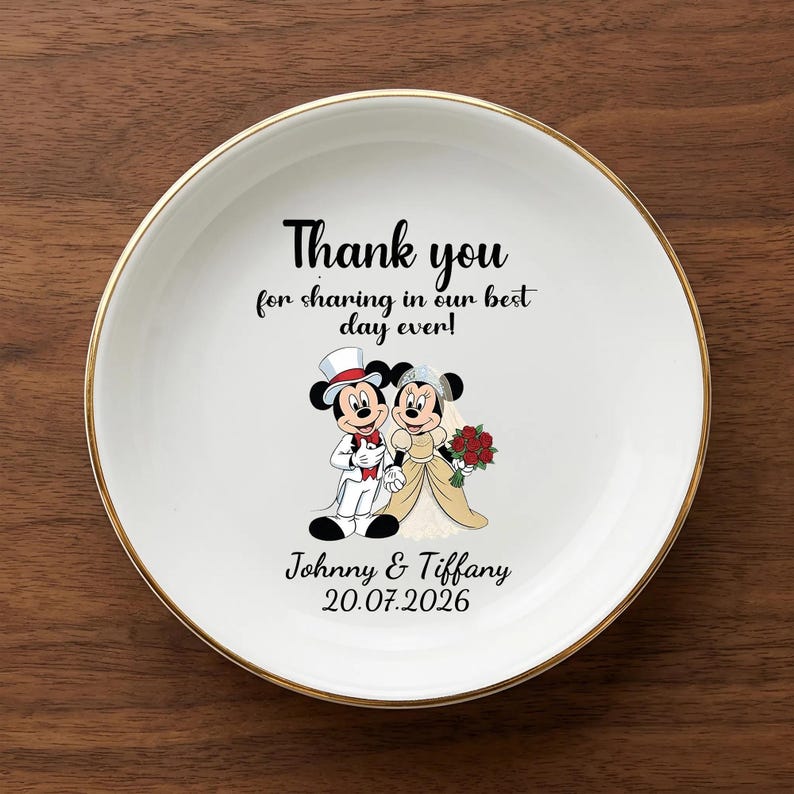 Puede incluir: Un plato de cer&aacute;mica blanco con borde dorado presenta una ilustraci&oacute;n de dibujos animados de Mickey y Minnie Mouse vestidos de novios. El plato incluye el texto "Thank you for sharing in our best day ever!" y los nombres "Johnny & Tiffany" con la fecha "20.07.2026".