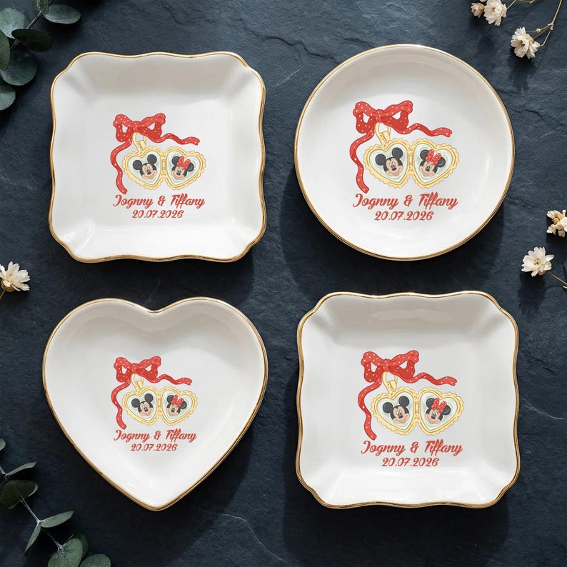 Op de afbeelding: Vier witte decoratieve schaaltjes met gouden rand, elk met een Mickey en Minnie Mouse ontwerp met een rode strik en de tekst "Jognny & Tiffany 20.07.2026". De schaaltjes hebben vierkante, ronde, hart- en geschulpte vierkante vormen.