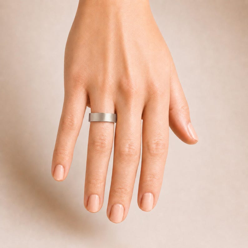 A close-up view of a person's hand wearing a silver ring on the ring finger.