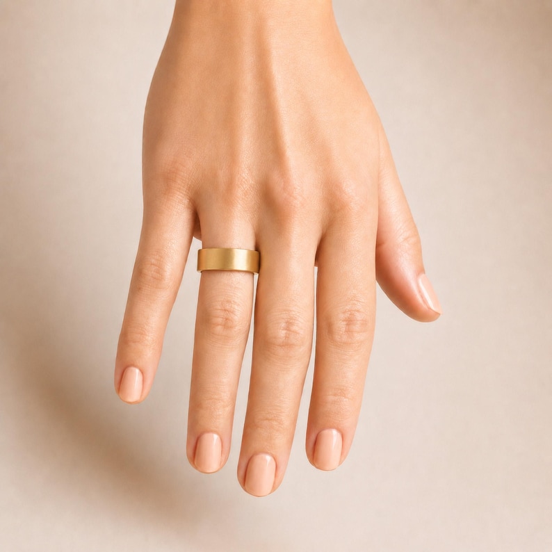 A close-up of a hand wearing a gold ring on the ring finger.