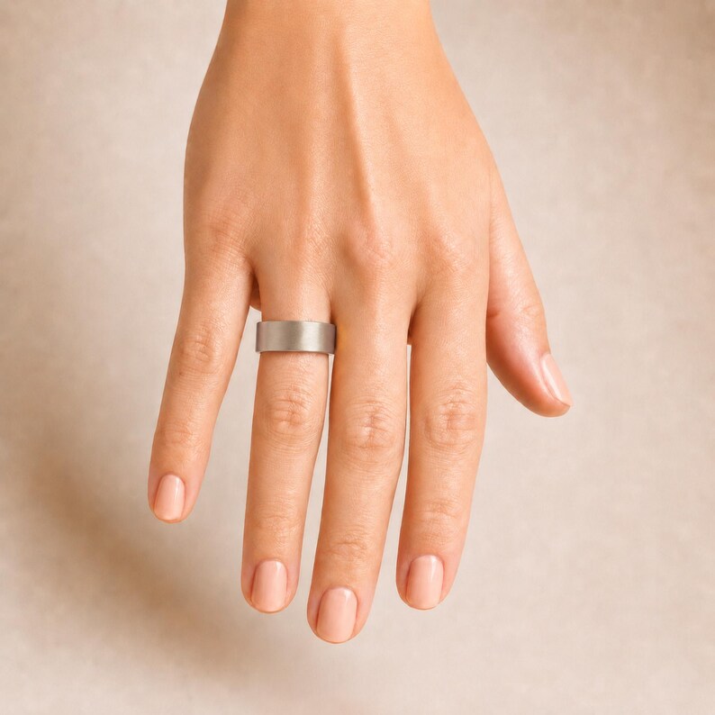 A close-up view of a person's hand wearing a silver ring on the ring finger.