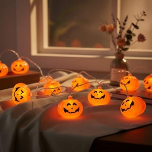 May include: A string of orange LED lights shaped like miniature jack-o'-lanterns with black painted facial features. The glowing pumpkin-shaped covers are connected by a thin wire, creating a festive illumination effect across the draped fabric.