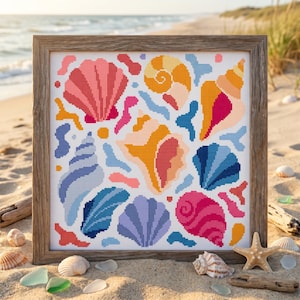 May include: A square cross-stitch embroidery featuring a colorful pattern of various seashells and coral shapes in shades of pink, orange, yellow, and blue, framed in a rustic brown wooden frame with a visible grid texture on the fabric.