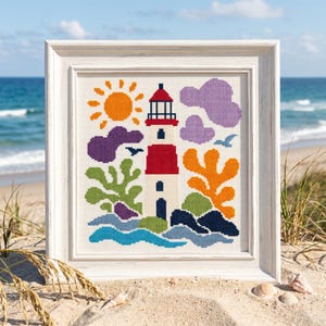 May include: A framed cross-stitch embroidery featuring a central lighthouse with a red and white tower, a bright orange sun, purple clouds, green and orange coral-like shapes, and blue waves, all rendered in a pixelated style on white fabric.