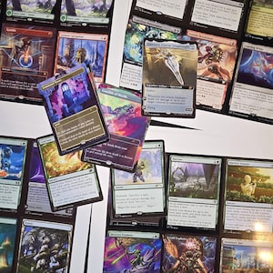 May include: A collection of Magic: The Gathering trading cards arranged on a white surface. The cards feature various illustrations, including landscapes, creatures, and artifacts, with printed text detailing game rules and card names.
