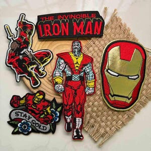 以下が含まれることがあります： コミックのキャラクターが描かれた刺繍パッチのコレクション。パッチには、アイアンマン、デッドプール、コロッサスが含まれています。1つのパッチには「THE INVINCIBLE IRON MAN」というテキストがあり、別のパッチには「STAY GOLD」と書かれています。