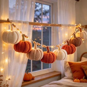 Puede incluir: Una guirnalda decorativa con calabazas de ganchillo en tonos crema, naranja y marrón, intercaladas con cuentas de madera e iluminadas por finas luces. Las calabazas presentan una textura con nervaduras verticales y tallos.