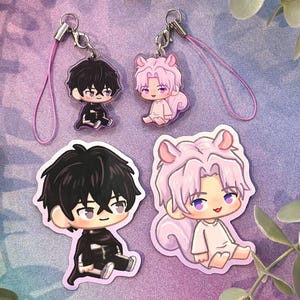 May include: Four anime-style character charms. Two charms feature a black-haired character in a black outfit, and two charms feature a pink-haired character in a white outfit. Each charm has a silver clasp and a pink lanyard.