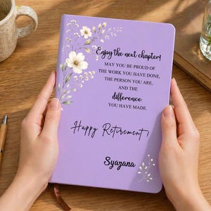 Op de afbeelding: Een lichtpaars notitieboek met een bloemenillustratie en zwarte tekst: Enjoy the next chapter! May you be proud of the work you have done, the person you are, and the difference you have made. Happy Retirement, Syazana.