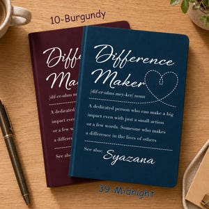 May include: Two rectangular notebooks in burgundy and midnight blue, each featuring the white printed text Difference Maker, a phonetic pronunciation, a definition of the term, and the name Syazana at the bottom with a heart graphic.