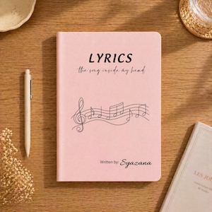 Könnte beinhalten: Ein rosa Notizbuch mit dem Wort "LYRICS" in fetten schwarzen Buchstaben oben und dem Satz "the song inside my head" darunter. Ein Notensystem mit Noten ist unter dem Text abgebildet. Der Name "Syazana" steht unten.