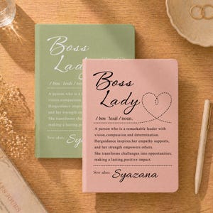 May include: Two rectangular notebooks, one sage green and one dusty pink, featuring the printed text Boss Lady, a dictionary-style definition, a dashed heart outline, and the name Syazana. A beige pen lies beside the pink notebook.