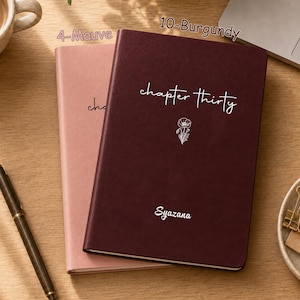 May include: Two hardcover journals in mauve and burgundy colors. The burgundy journal features the white text "chapter thirty" above a small floral line drawing and the name "Syazana" at the bottom. The mauve journal is partially visible behind it.
