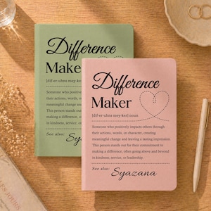 May include: Two notebooks, one sage green and one blush pink, with the words "Difference Maker" and "Difference Make" in elegant script. The pink notebook features a heart design and a definition. A pen and a dish with rings are also visible.