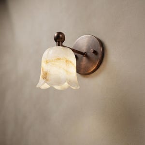 May include: A wall-mounted light fixture featuring a round, dark bronze-toned metal base and a single arm extending to a bell-shaped, translucent white and amber marbled glass shade. The text Texas Brass Lights is visible in the bottom right corner.