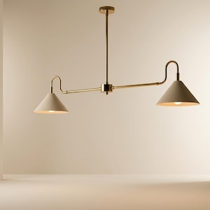 May include: A linear pendant light fixture featuring a central brass rod and two adjustable arms extending horizontally. Each arm holds a matte off-white conical shade with a downward-facing light source. The fixture is suspended by a single vertical brass stem.