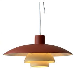 May include: A pendant light fixture featuring a large, matte rust-red circular shade at the top, with two smaller, nested, light-colored cream-toned dome shades underneath. The lamp is suspended by a single white cord extending from the top center.