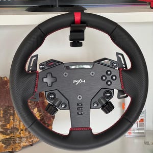 May include: A black racing steering wheel controller featuring a perforated leather grip with red stitching, a central brushed metal faceplate with the PXN logo, integrated buttons, a directional pad, and paddle shifters mounted behind the wheel rim.