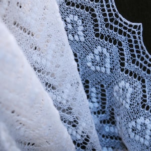 Puede incluir: Primer plano de una delicada tela de encaje blanco, que muestra intrincados patrones florales y geométricos. El material suave y fluido está en capas, creando profundidad y textura. El encaje se utiliza probablemente para chales, bufandas u otros artículos decorativos.