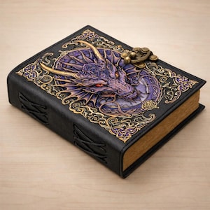 May include: A black leather journal with a dragon design on the cover. The dragon is purple and gold, with red eyes. The cover features gold filigree and a brass clasp. The pages have a golden hue.