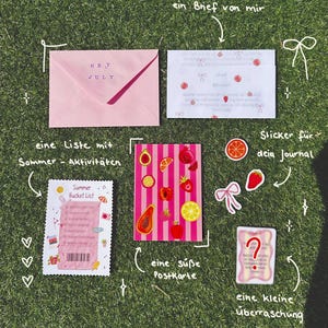 Könnte beinhalten: Ein Schreibwarenset bestehend aus einem rosa Umschlag mit der Aufschrift HEY JULY, einem weißen Brief mit roten Fruchtmustern, einer Summer Bucket List Karte, einer Postkarte mit rosa Streifen und Früchten, drei Stickern und einer Überraschungskarte.