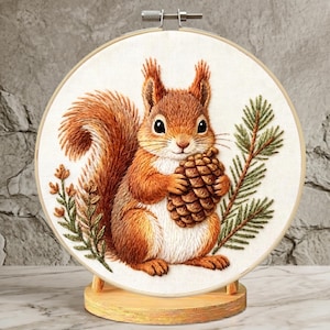 May include: Embroidered artwork featuring a detailed squirrel holding a pinecone, set against a backdrop of greenery. The squirrel has reddish-brown fur and is centered in a round wooden embroidery hoop. The artwork is displayed on a wooden stand.