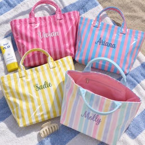 Peut inclure: Quatre sacs fourre-tout rectangulaires à rayures verticales roses, bleues, jaunes et pastel. Chaque sac porte un prénom brodé : Vivian, Ariana, Sadie et Molly. Les sacs ont deux anses supérieures et une finition lisse et brillante.