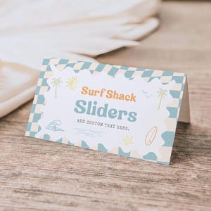 May include: A folded rectangular card with a light blue and cream checkered border. The center features the text Surf Shack Sliders and ADD CUSTOM TEXT HERE, surrounded by small illustrations of a sun, palm trees, a wave, a starfish, and a surfboard.