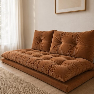 May include: A low-profile floor sofa upholstered in a rust-coloured velvet fabric. The piece features two large, tufted back cushions and a thick, tufted seat cushion, all resting on a matching rectangular base platform with a soft, plush texture.