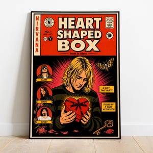 May include: A framed poster featuring a comic book style design with the text "HEART SHAPED BOX" and the band name "NIRVANA". The artwork includes illustrations of band members, a heart-shaped box, and a key. The color palette is dominated by red, black, and yellow.