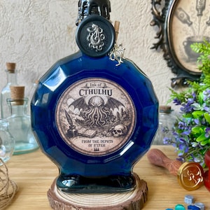 Peut inclure: Une bouteille en verre bleu foncé, facettée, avec un sceau de cire noir et l'inscription "Ink of Cthulhu" sur une étiquette. La bouteille repose sur une petite base en bois. L'étiquette présente une illustration.