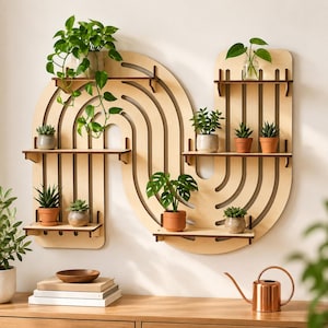 Puede incluir: Una estantería de pared de madera clara con un diseño curvo en forma de arco y múltiples plataformas horizontales. La estantería sostiene varias plantas verdes pequeñas en macetas, incluyendo una enredadera, suculentas y una pequeña monstera en macetas de terracota.