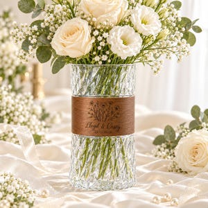 May include: A clear glass vase with a textured, diagonal ribbed pattern and a central horizontal wooden band. The wood features an engraved floral illustration, the text "Lloyd & Casey," and the date "25.11.2026" in a dark, elegant script font.