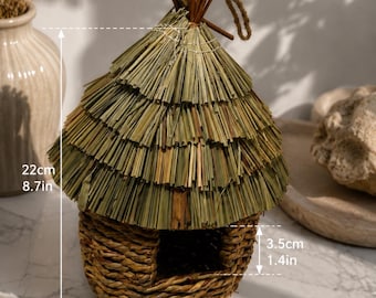 May include: A woven grass birdhouse with a conical thatched roof and a square entrance. The structure measures 8.7 inches in total height, 6.7 inches in width, and the entrance opening is 1.4 inches high. A jute rope loop is attached to the top.