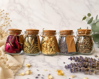 May include: Five small glass jars with cork stoppers, each filled with different dried botanicals including red rose petals, green lemongrass, yellow jasmine flowers, purple lavender buds, and grey sage leaves, with a brown paper tag tied to each.