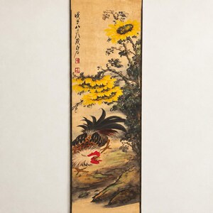 May include: A vertical hanging scroll painting on tan paper featuring a rooster with black, white, and red plumage standing near a cluster of bright yellow sunflowers with dark green leaves. Black ink calligraphy and two red square seals are visible.