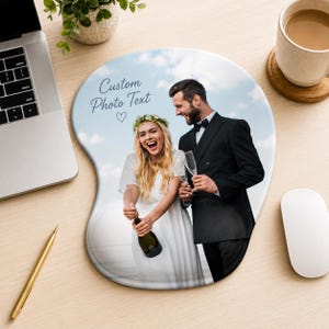 May include: A custom mouse pad featuring a printed photograph of a person in a white dress and a person in a black suit holding champagne glasses, with the text "Custom Photo Text" and a heart icon printed in the upper left corner of the pad.