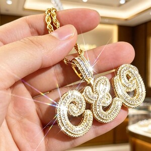 Pode incluir: Um colar com pingente em tom dourado apresentando as letras "CEO" em letra cursiva. O pingente é incrustado com inúmeras pequenas pedras transparentes de corte baguette que criam um efeito cintilante. Pendurado em uma corrente de corda.