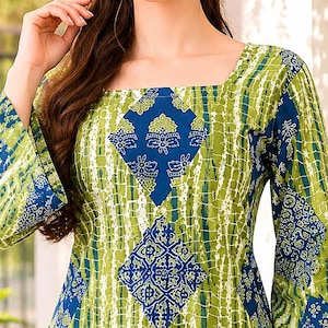 Op de afbeelding: Een tuniek met lange mouwen en een vierkante halslijn, voorzien van een levendig patroon van verticale limoengroene strepen afgewisseld met blauwe ruitvormige panelen met gedetailleerde witte bloemmotieven en geometrische patronen, gecombineerd met een witte broek.