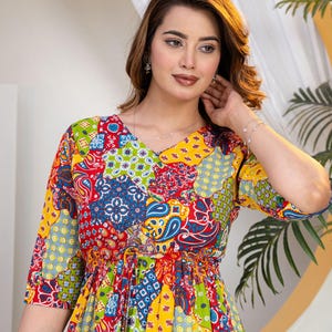 Puede incluir: Un vestido con un vibrante patrón de retazos multicolor que incluye motivos de cachemira, florales y geométricos en tonos rojo, amarillo, azul y verde. La prenda tiene cuello en V, mangas tres cuartos y una cintura ajustada con cordón.