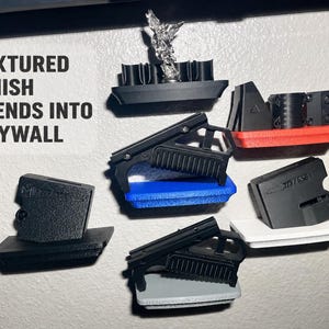 Puede incluir: Una colección de soportes negros para accesorios de armas de fuego con bases texturizadas en varios colores, incluyendo rojo, azul, blanco y gris. El texto "TEXTURED FINISH BLENDS INTO DRYWALL" está impreso a la izquierda. Estos soportes presentan diversas formas.