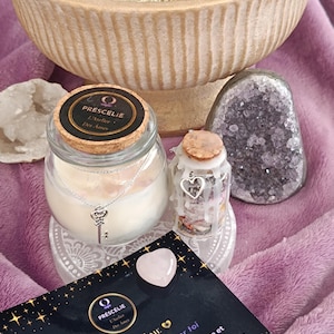 Peut inclure: Une bougie dans un bocal en verre avec un couvercle en liège, une petite bouteille en verre, un quartz rose en forme de cœur et une carte avec du texte. Un pendentif clé en argent est suspendu au bocal à bougie.