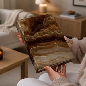 May include: A rectangular box featuring a polished brown and cream onyx stone finish with natural swirling patterns. The object has a smooth, glossy surface with distinct horizontal banding in shades of dark chocolate, tan, and translucent off-white.