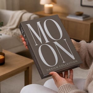 Op de afbeelding: Een rechthoekig boek met een donkerbruine kaft met de grote witte tekst MOON en de kleinere witte tekst DESIGN COLLECTION op de voorkant. De rug van het boek toont ook het woord MOON in witte hoofdletters.