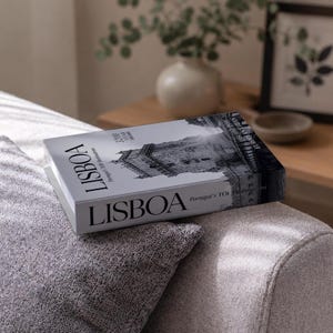 Pode incluir: Um livro retangular intitulado LISBOA com uma fotografia a preto e branco de uma torre de pedra histórica na capa. O texto na capa inclui LISBOA, Portugal's TOP Destinations, 3200 YEAR HISTORY e DISCOVERING EUROPEAN CITIES em fonte preta.