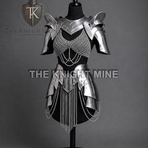 May include: A silver metal armour set displayed on a black mannequin. The armour includes shoulder pauldrons, a chest piece with chainmail, and a skirt-like lower section. The text "THE KNIGHT MINE" is visible.
