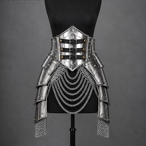May include: A polished silver metal waist armour piece featuring a pointed front plate secured with three black leather straps and brass buckles. The design includes layered side plates, hanging chain drapes, and chainmail fringe at the bottom edges.