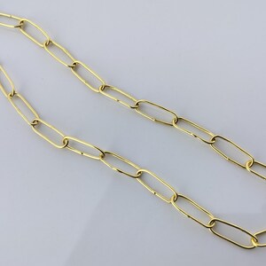 Könnte beinhalten: Eine goldfarbene Kettenhalskette mit länglichen, rechteckigen Gliedern, die in einer durchgehenden Schleife verbunden sind. Das Metall hat eine polierte, reflektierende Oberfläche und das Design besteht aus einheitlichen, offenen Gliedern.