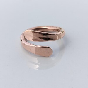 Peut inclure: Une bague en or rose au design ouvert unique. La bague s'enroule autour du doigt avec une finition lisse et polie. La bande a une forme plate et rectangulaire aux extrémités, créant une esthétique moderne et minimaliste.